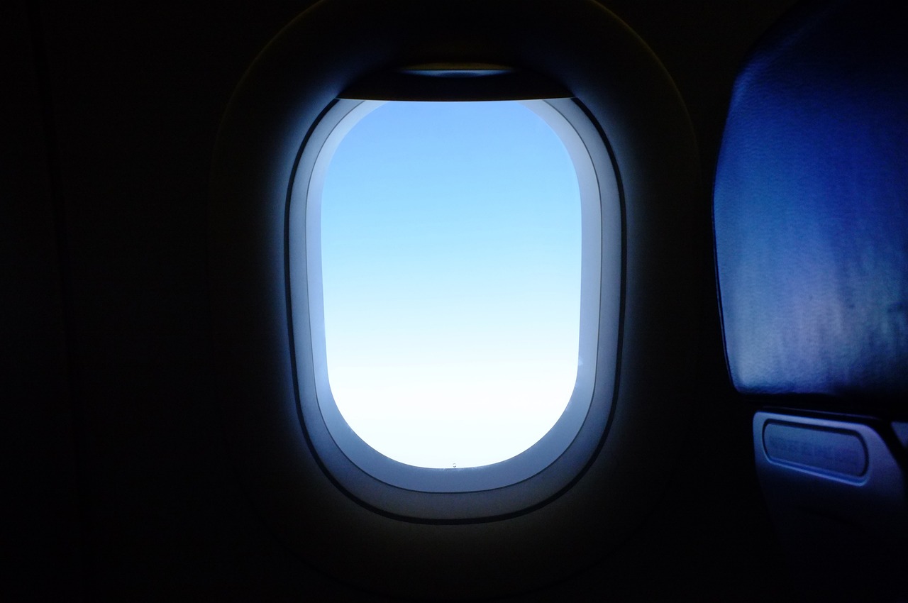 Uitzicht vanuit een vliegtuigraam tijdens een vlucht, met een vluchtschema zichtbaar op een scherm